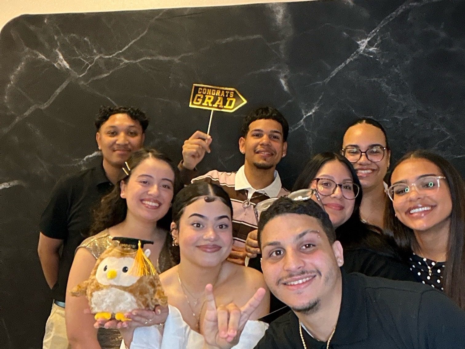 A group of guests crowded into one frame holding a Congrats Grad sign