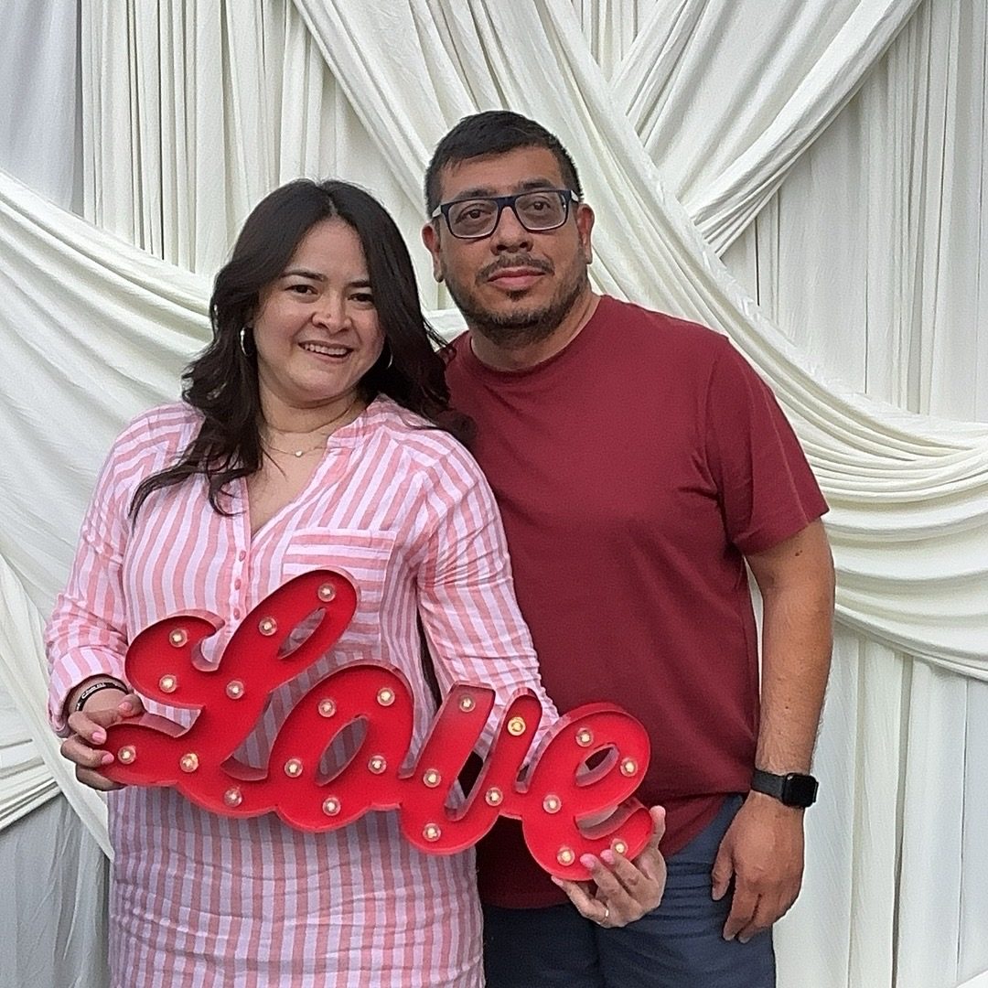 A couple holding a lit Love sign in front of an ivory draped backdrop