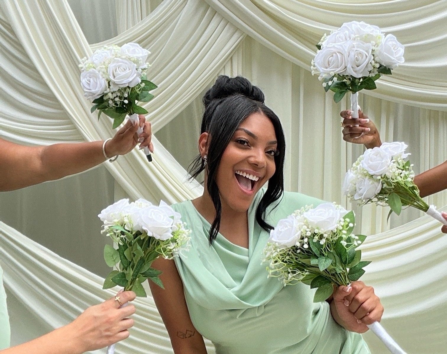 A guest laughing as bouquets are held up around her in front of ivory draping