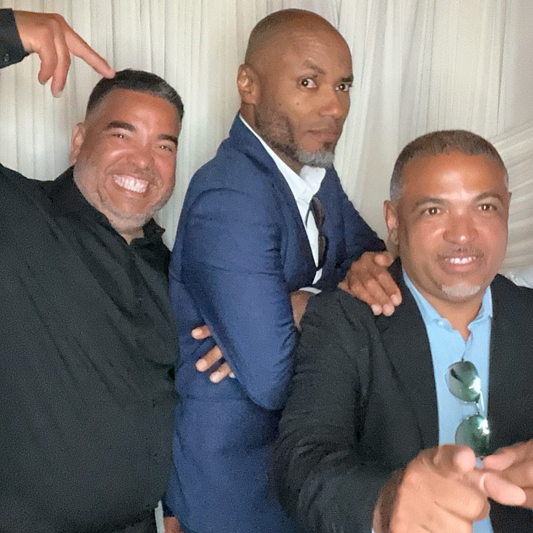 Three guests in suits leaning into one frame in front of ivory draping